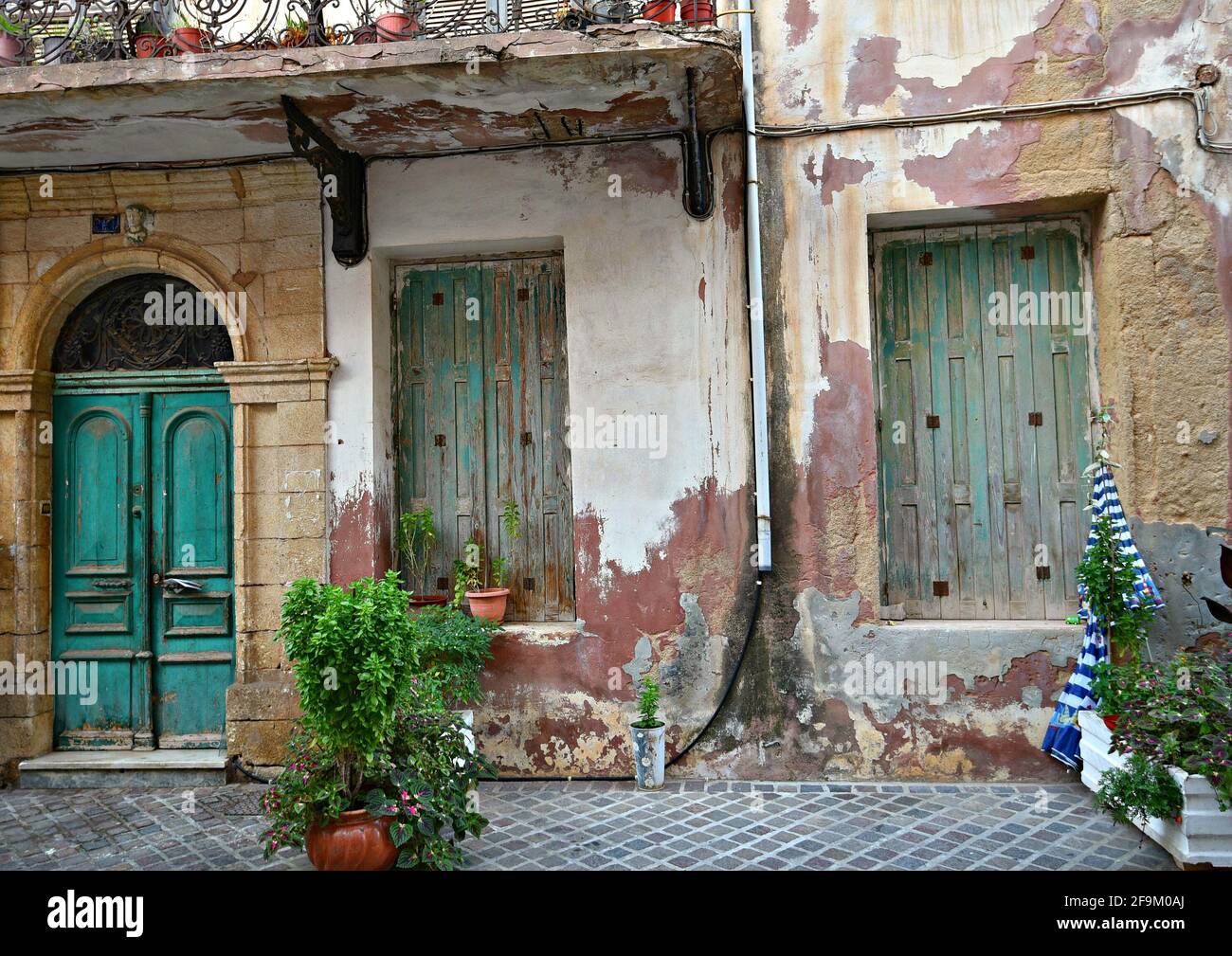 Old abandoned rural house facade with a faded wall and weathered wooden door and shutters in Chania, Crete island Greece. Stock Photo