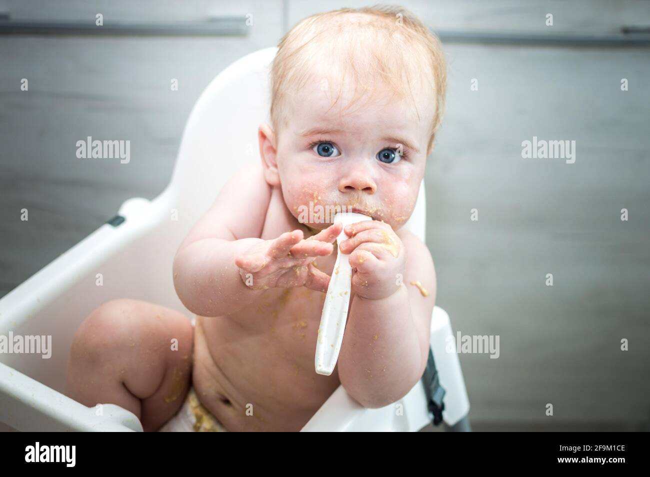 Closeup portrait of a child stained with food. The child is fed from a spoon in a highchair. Real life Stock Photo