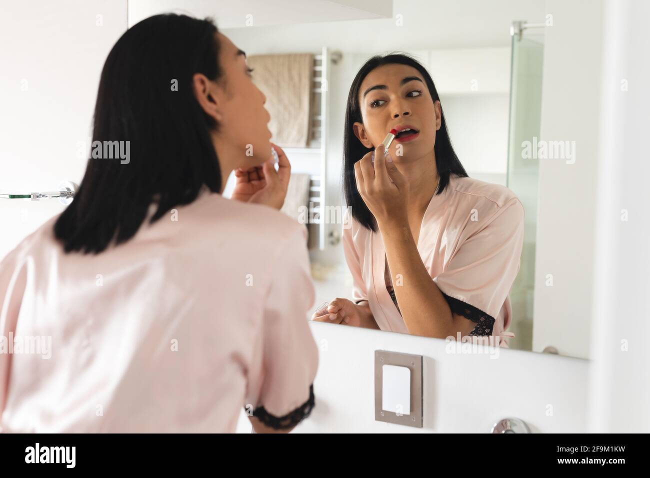 Mixed race transgender woman looking in bathroom mirror and putting on lipstick Stock Photo - Alamy