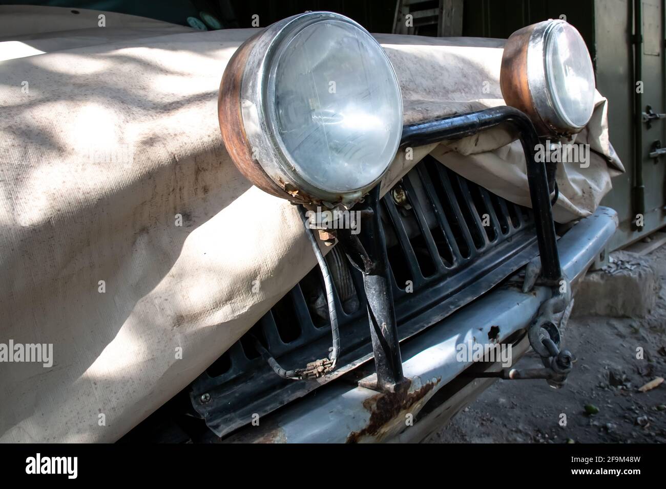 An old-fashioned off-roading vehicle covered with a beige tarpaulin canvas cover and external halogen head light bulbs on a light bar bumper. Stock Photo