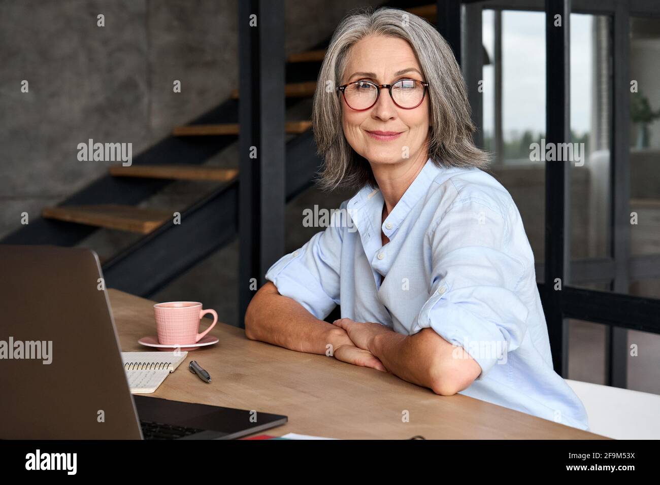 Portrait of smiling business woman 60s aged working at home with laptop. Stock Photo