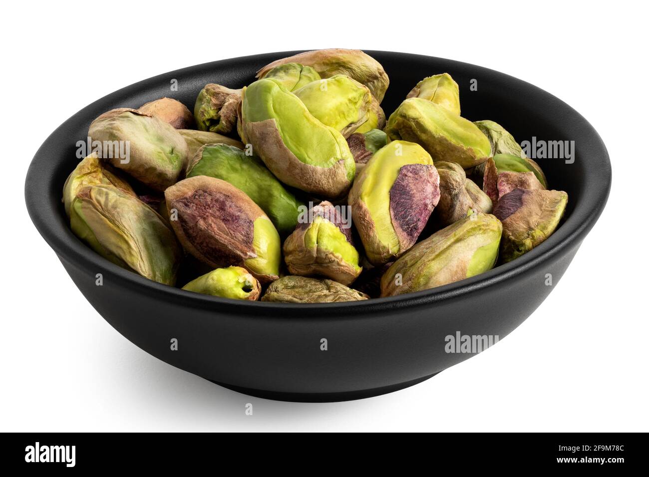 Shelled pistachios in a black ceramic bowl isolated on white. Stock Photo