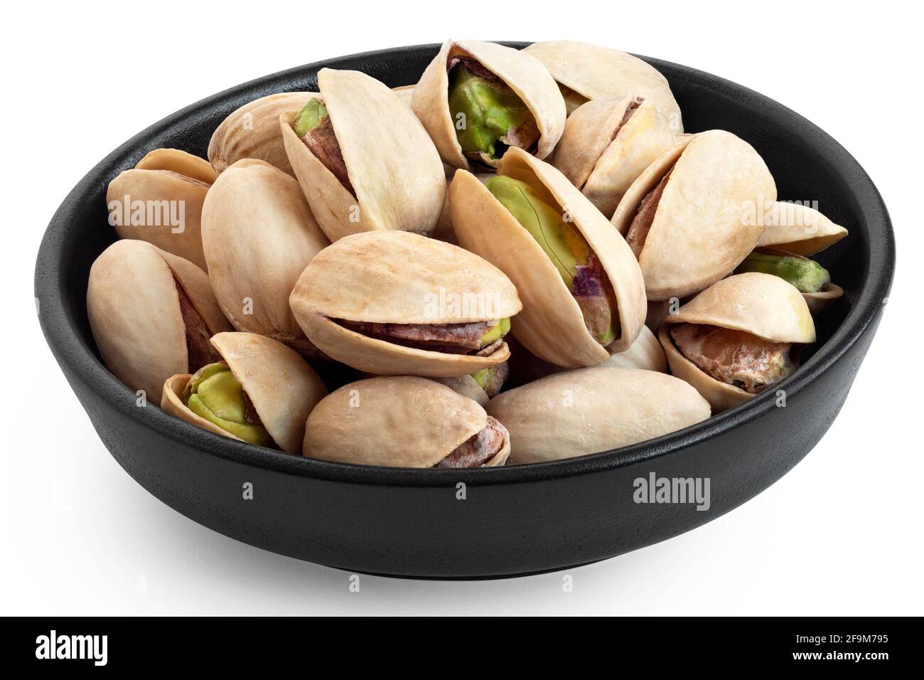 Salted pistachios in shell in a black ceramic bowl isolated on white. Stock Photo