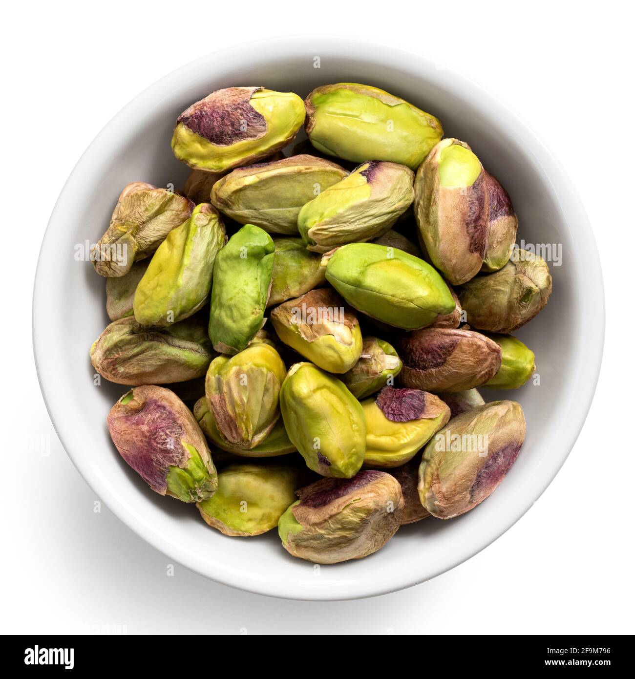 Shelled pistachios in a white ceramic bowl isolated on white. Top view. Stock Photo