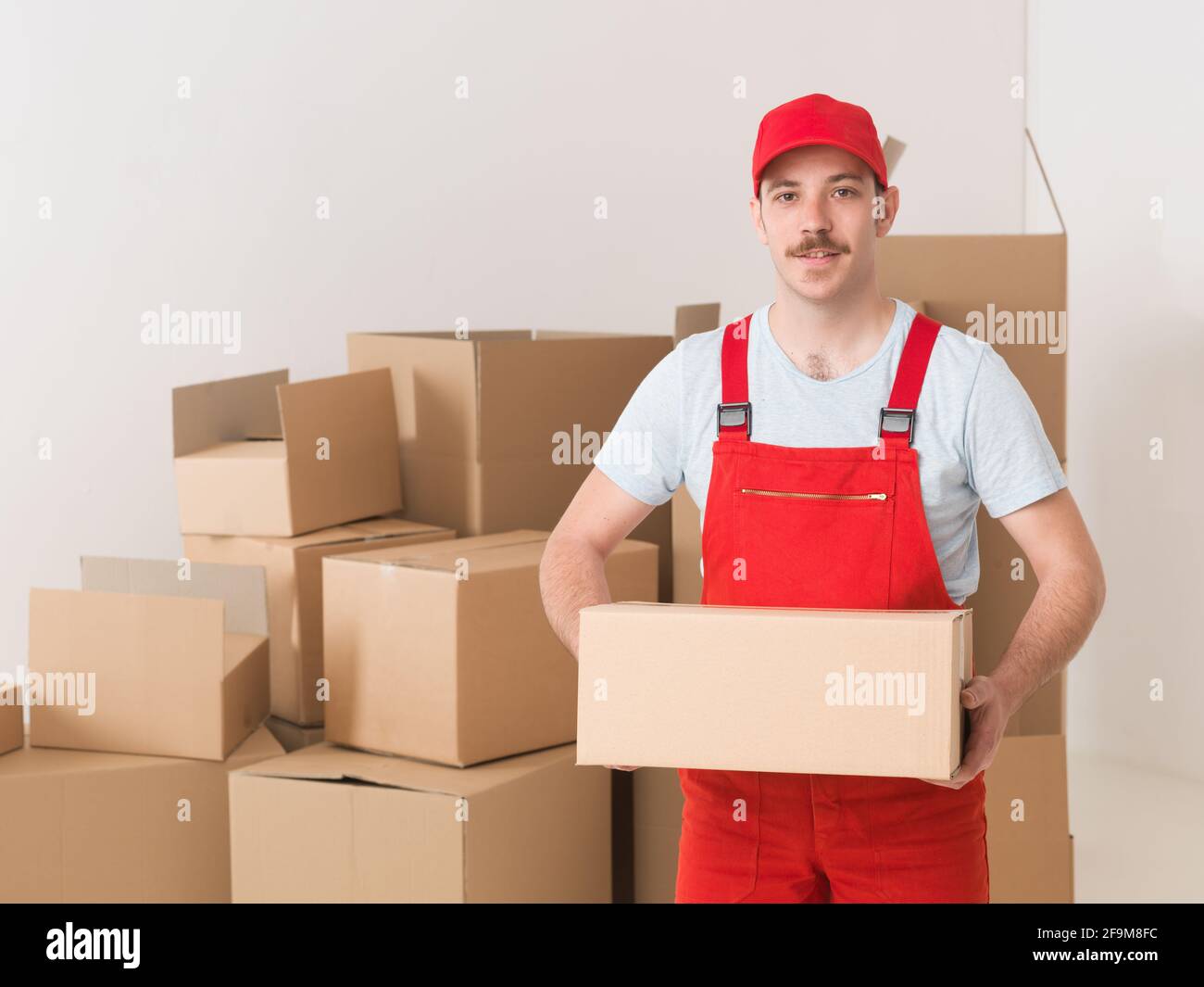 young caucasian deliveryman standing in warehouse, holding parcel Stock Photo