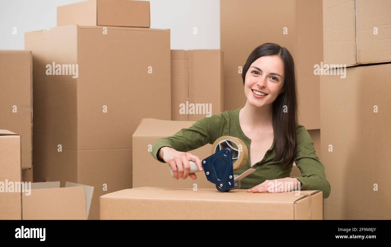 young caucasian woman sealing a cardboard box with adhesive tape. moving home Stock Photo