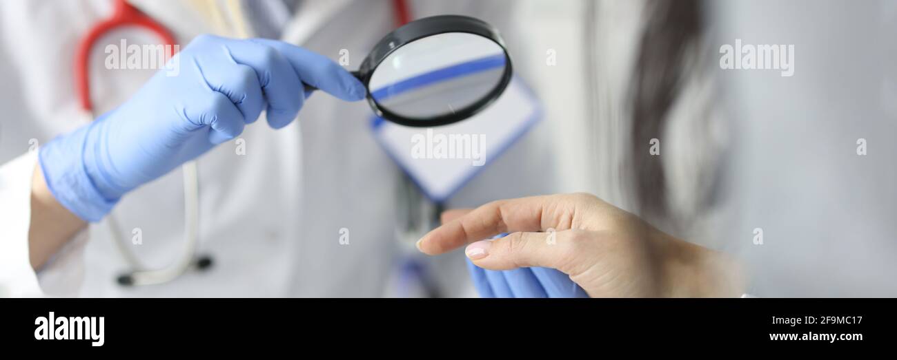 Dermatologist doctor looking at patients skin on hands using magnifying glass in clinic closeup Stock Photo