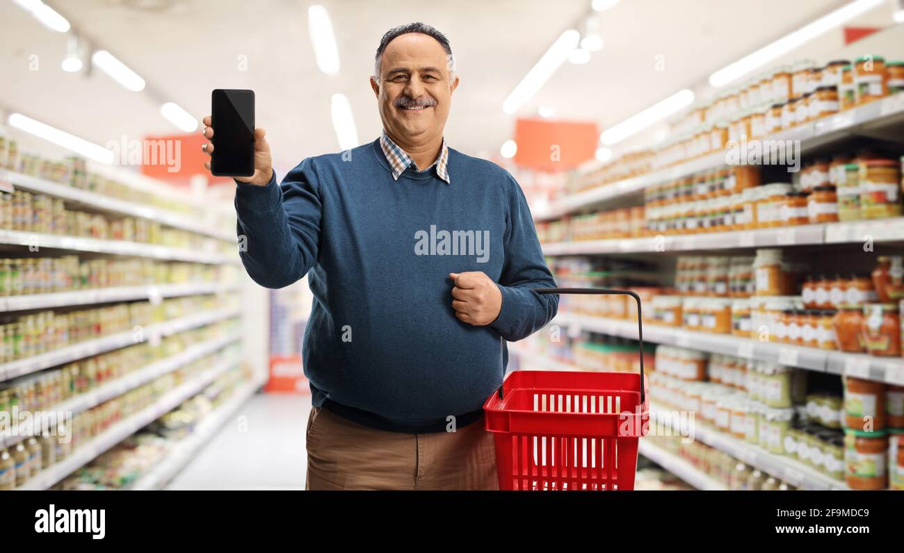 Satisfied mature male customer in a supermarket showing a mobile phone Stock Photo