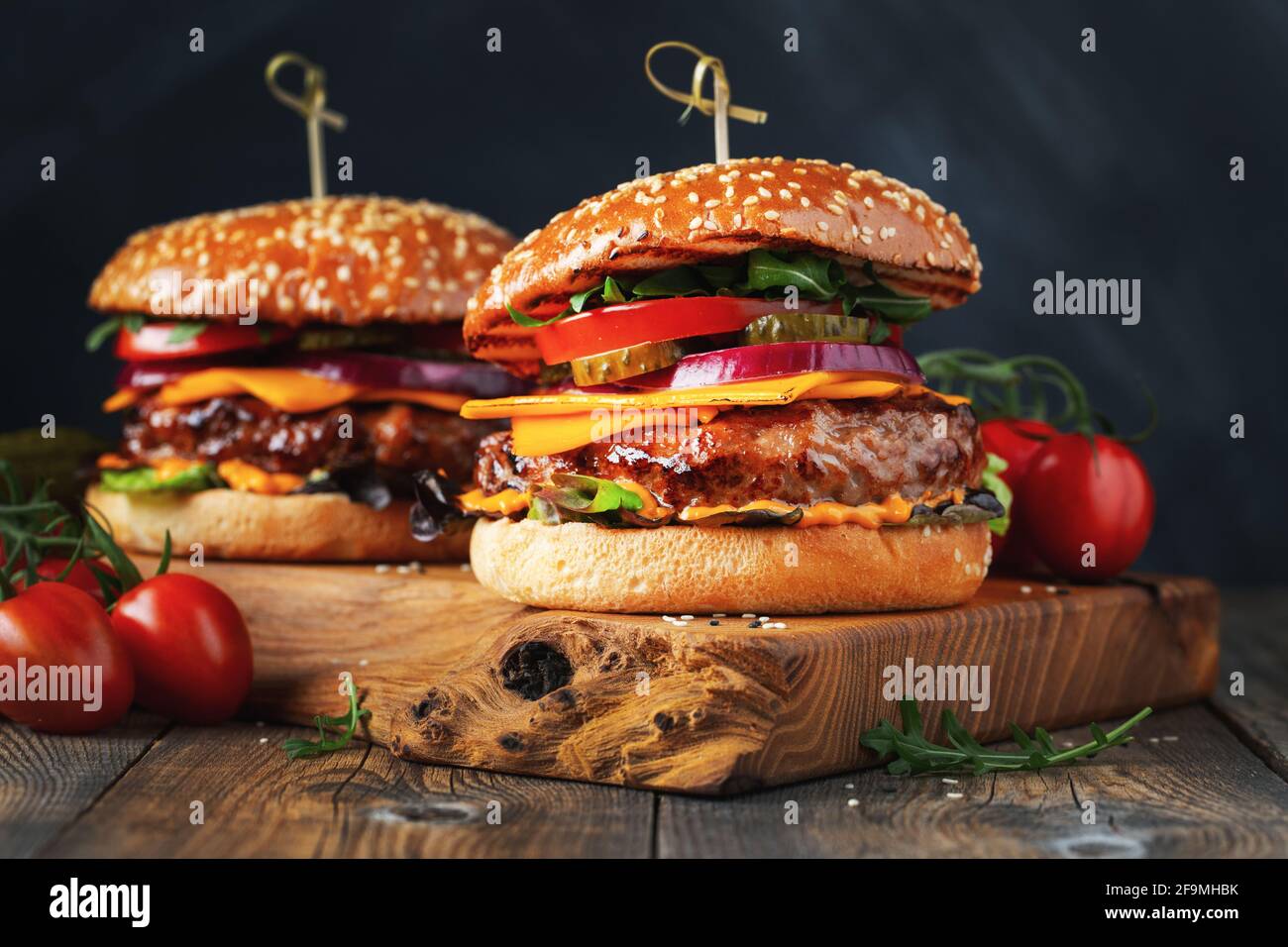 Two delicious homemade burgers of beef, cheese and vegetables on an old wooden table. Fat unhealthy food close-up Stock Photo