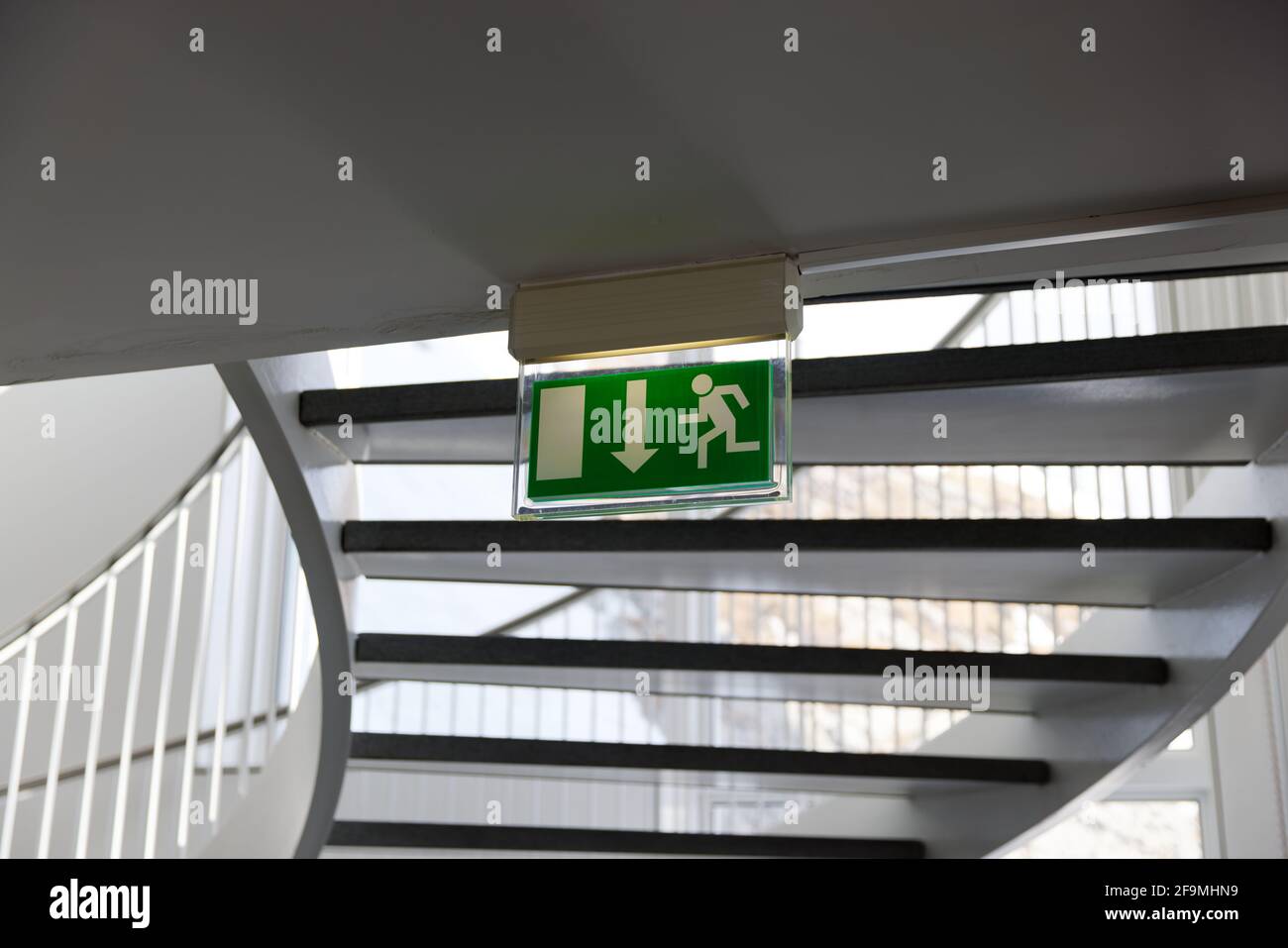 green emergency exit sign under a spiral staircase with railing, by day