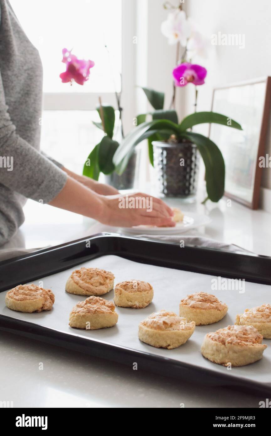 Blurred woman put cookie to a plate from baking sheet against th Stock Photo