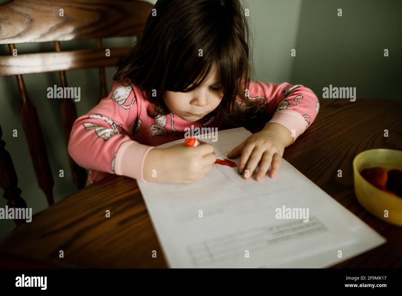 Young girl wearing pajamas coloring with a red marker at kitchen table Stock Photo