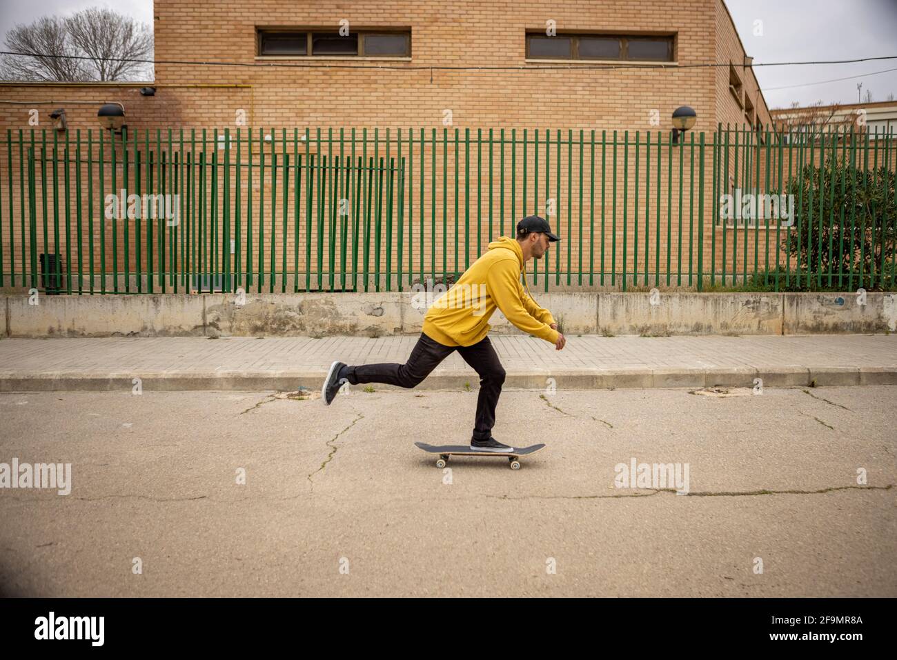 A young male skateboarding on the street in a yellow hoodie and a black cap Stock Photo