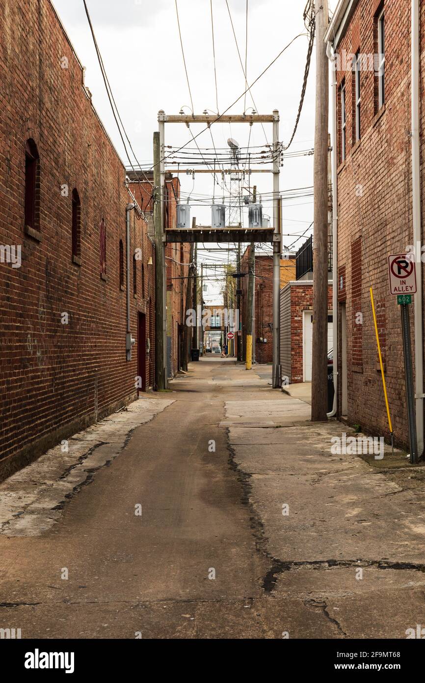 KINGSPORT, TN, USA--8 APRIL 2021: An empty alley in downtown Kingsport, with broken concrete and power transformers overhead.  Two people walking. Stock Photo