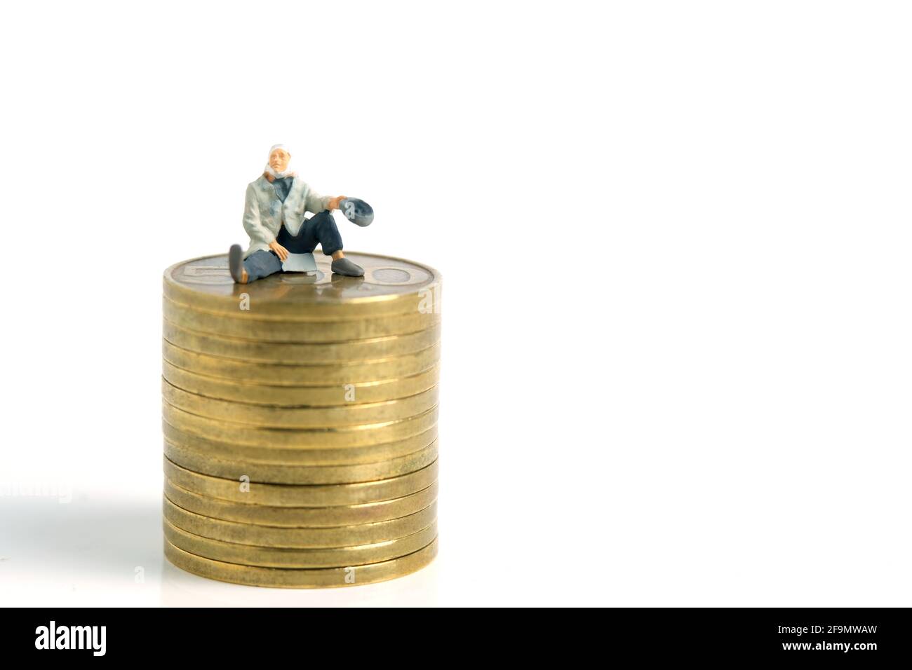 Miniature tiny people toys photography. A poor man or a beggar sit above gold coin stack, isolated on white background Stock Photo
