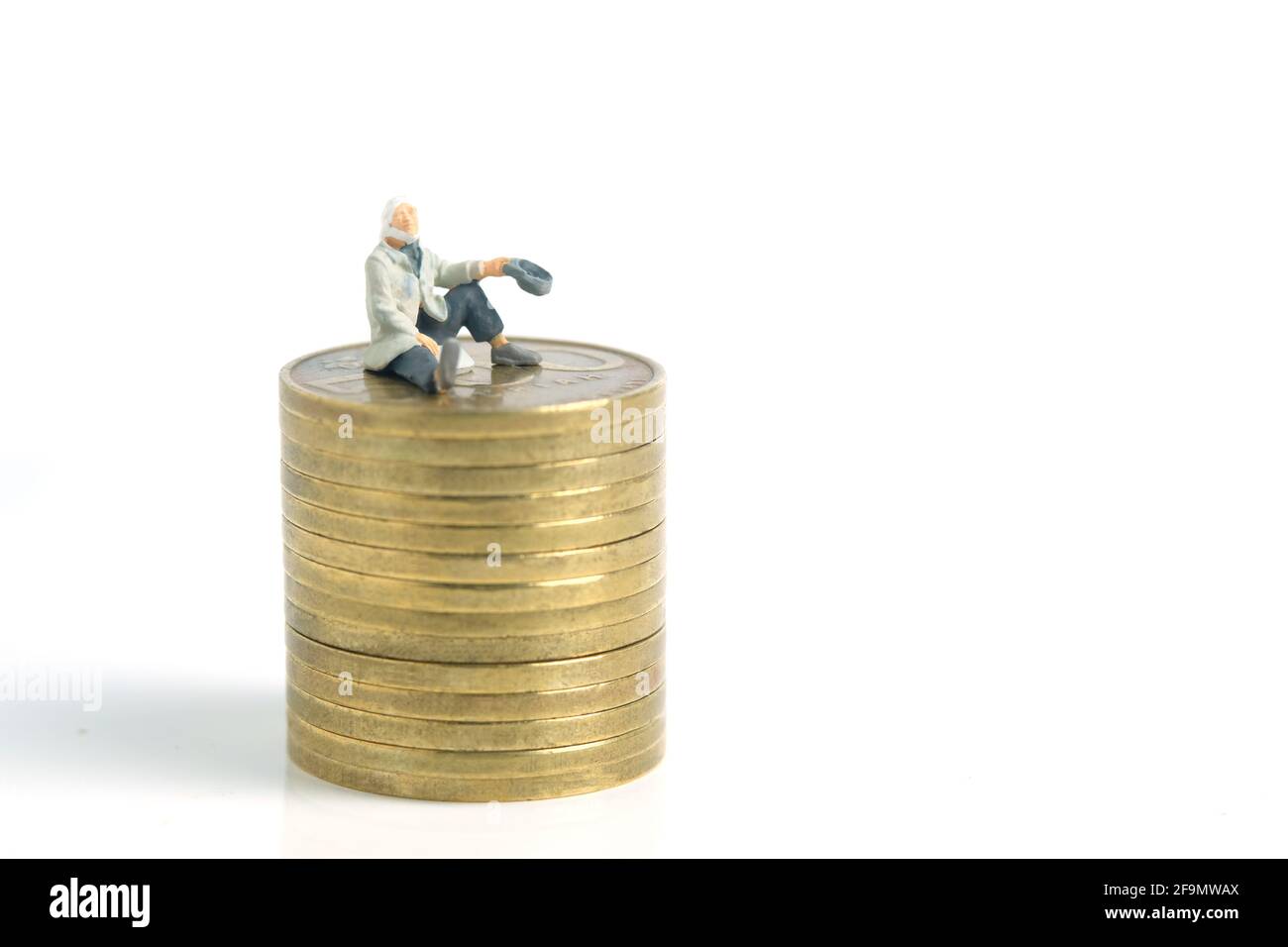 Miniature tiny people toys photography. A poor man or a beggar sit above gold coin stack, isolated on white background Stock Photo