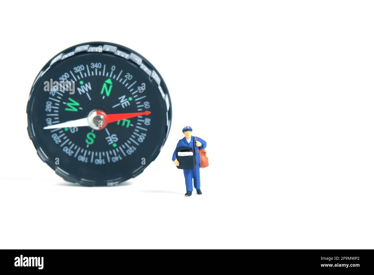 Miniature people toys conceptual photography. Address navigation. Postman courier with a compass, isolated on blue background. Stock Photo
