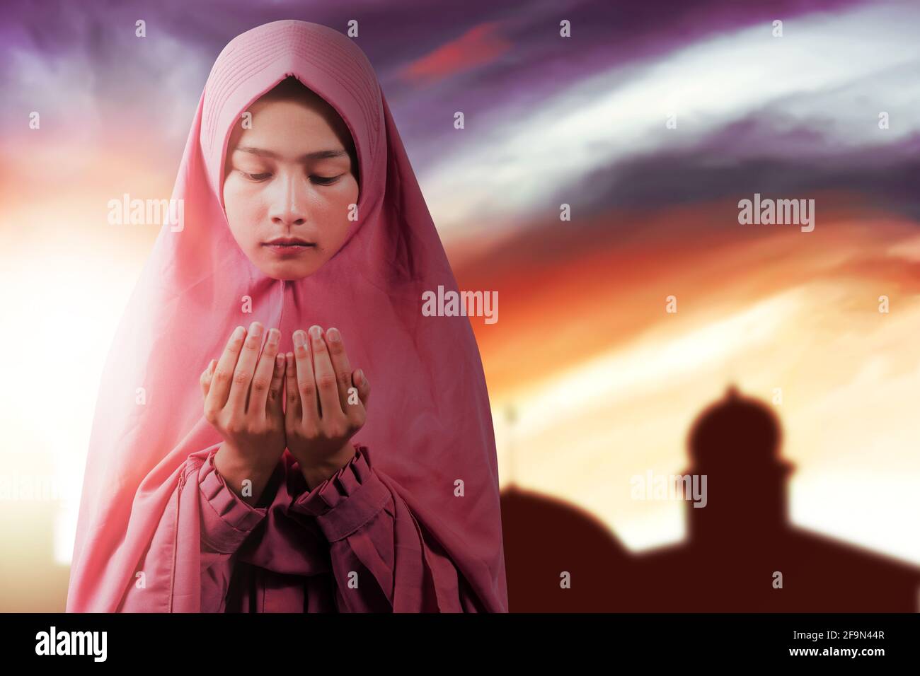 Asian Muslim woman in a veil standing while raised hands and praying ...