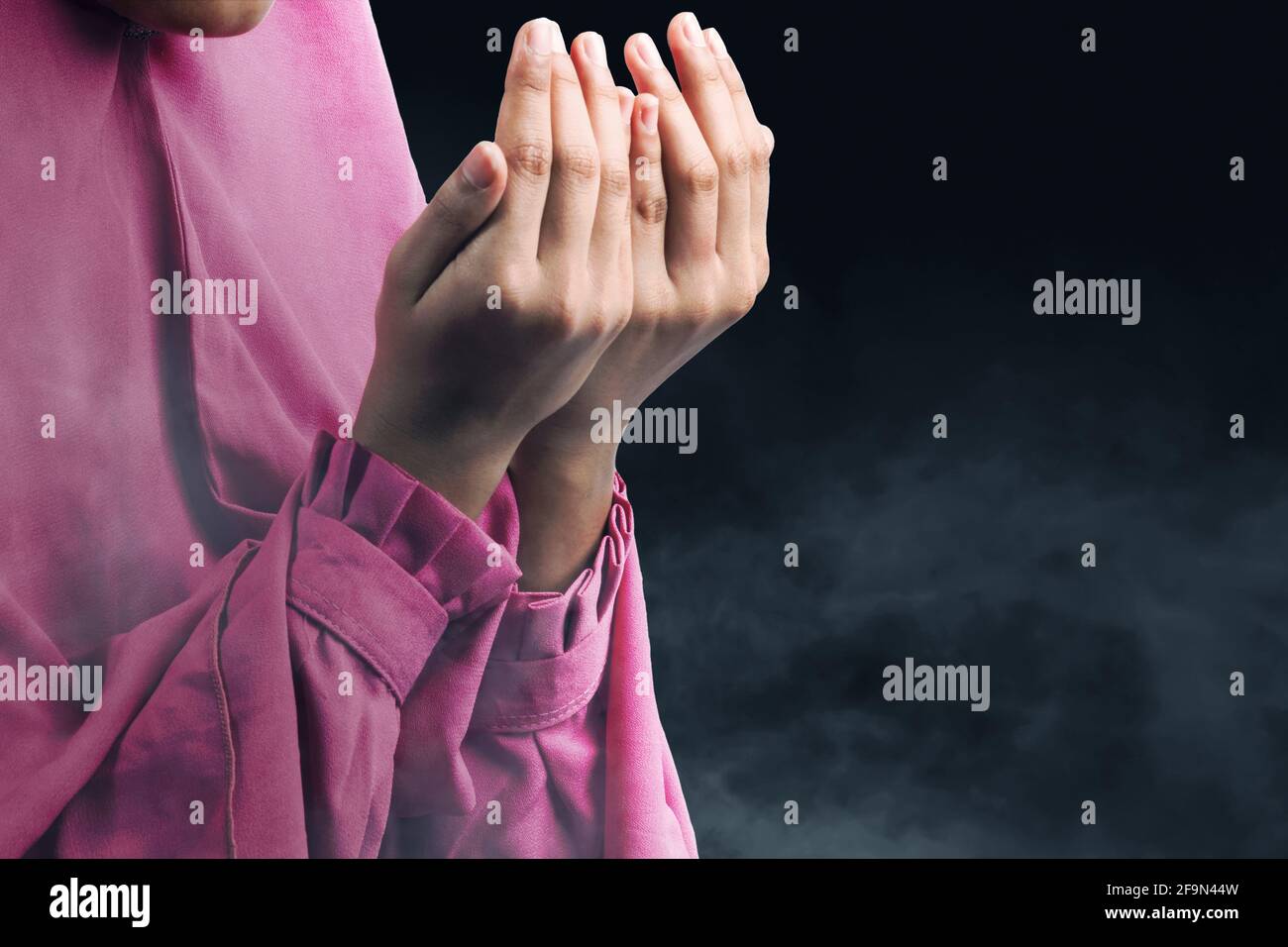 Muslim woman in a veil standing while raised hands and praying with ...