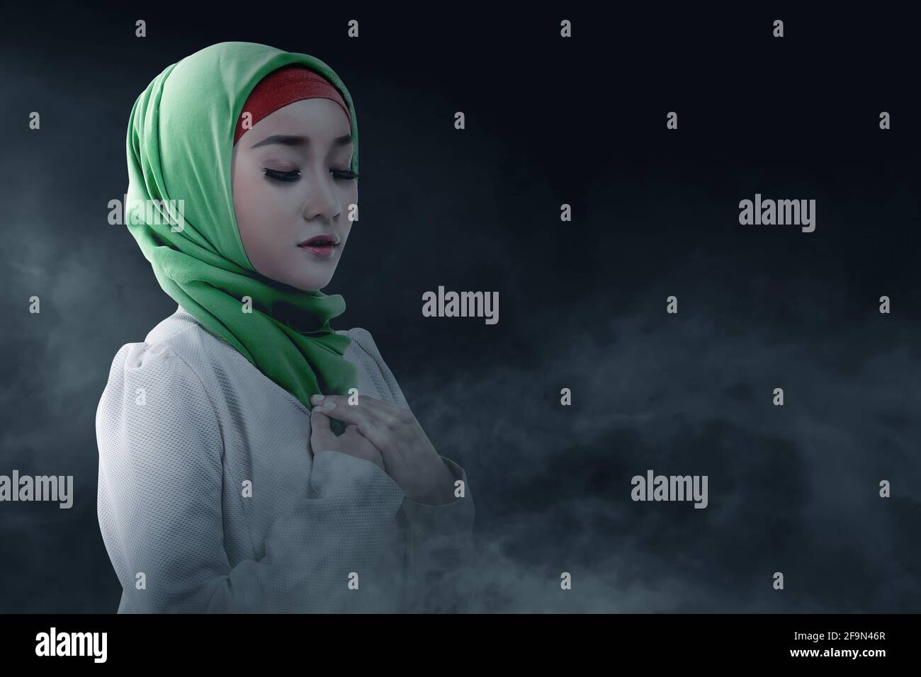 Asian Muslim woman in a veil standing while raised hands and praying ...
