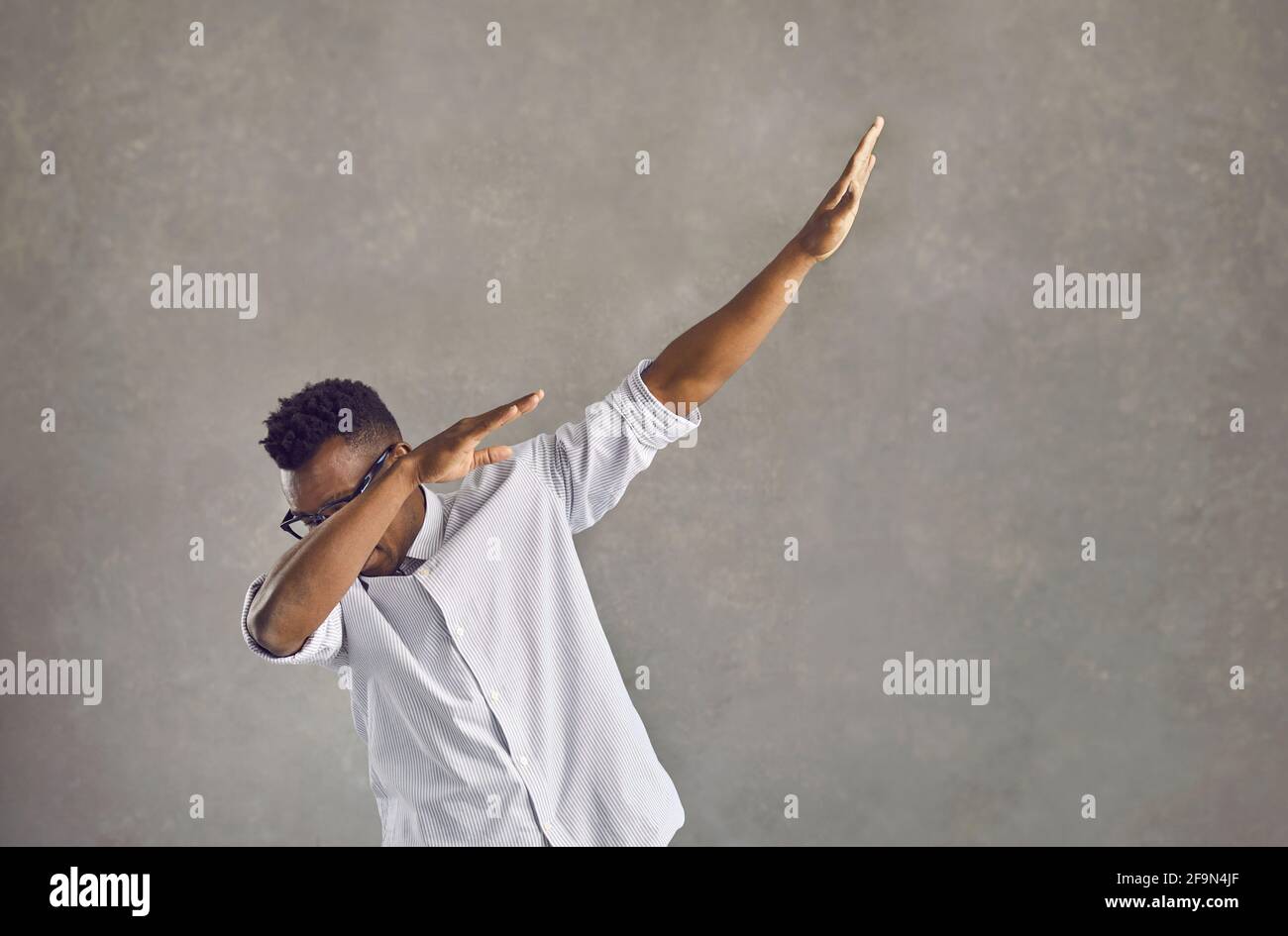 young black man doing popular dab dance move isolated on gray concrete background 2F9N4JF