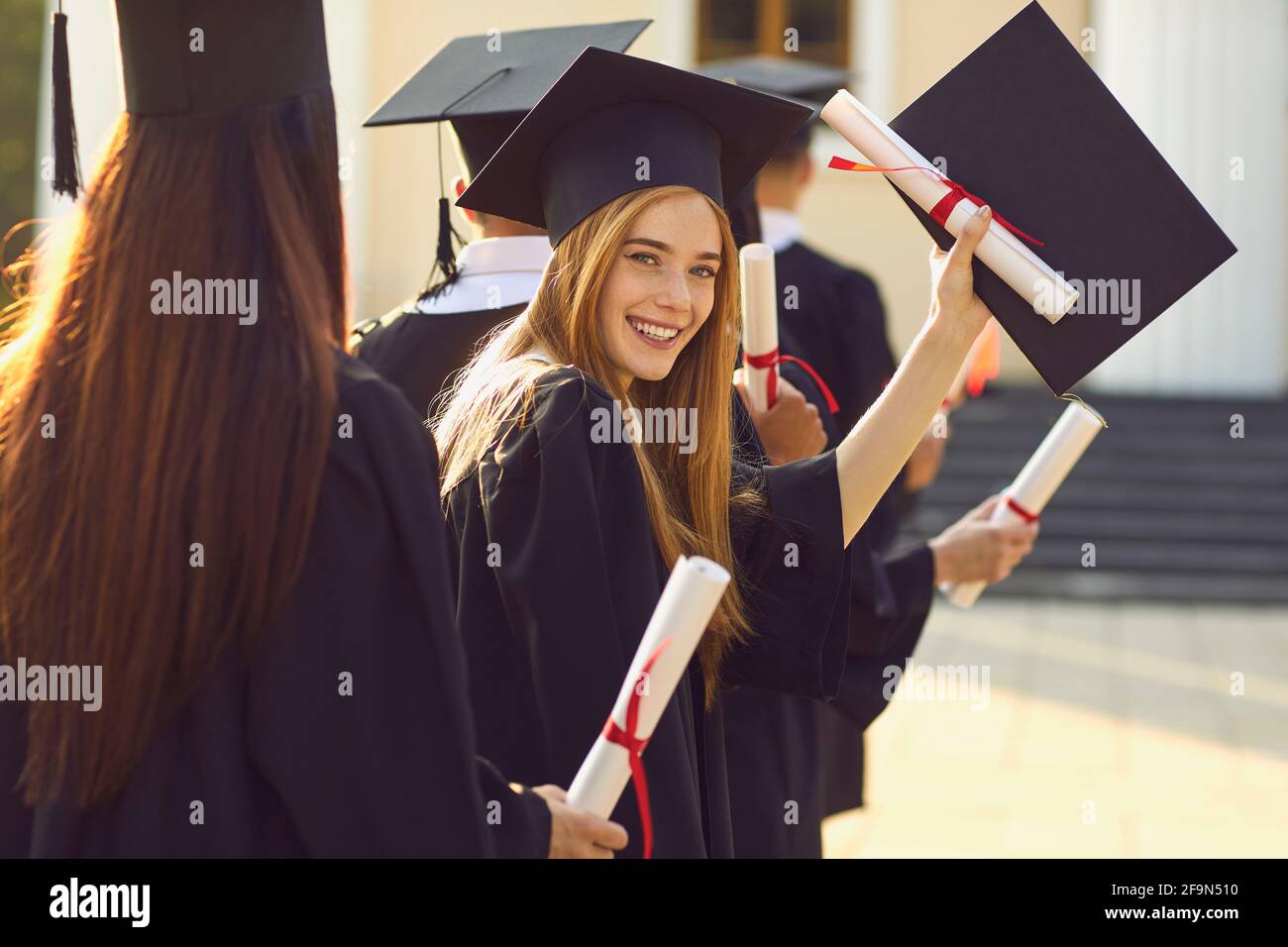 Smiling beautiful girl university or college graduate standing with diploma and looking at camera Stock Photo