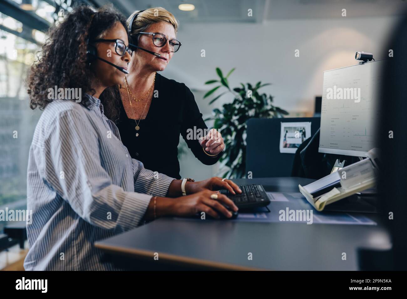 Two female coworkers cooperating while using computer and working in the office. businesswomen working together on a project in office. Stock Photo