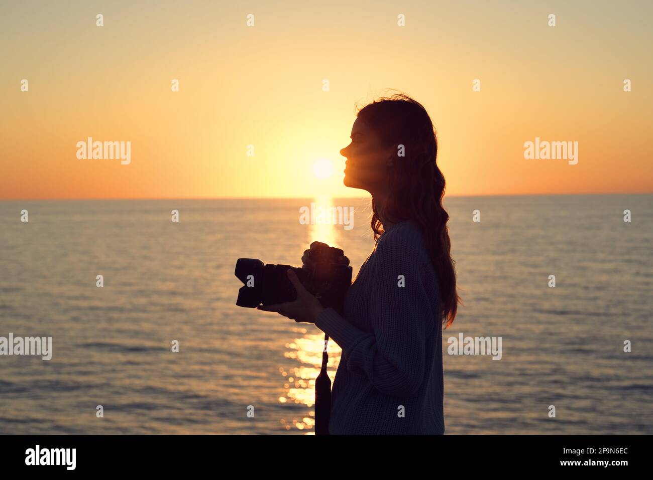 silhouette of a woman with a camera at sunset near the sea side view ...