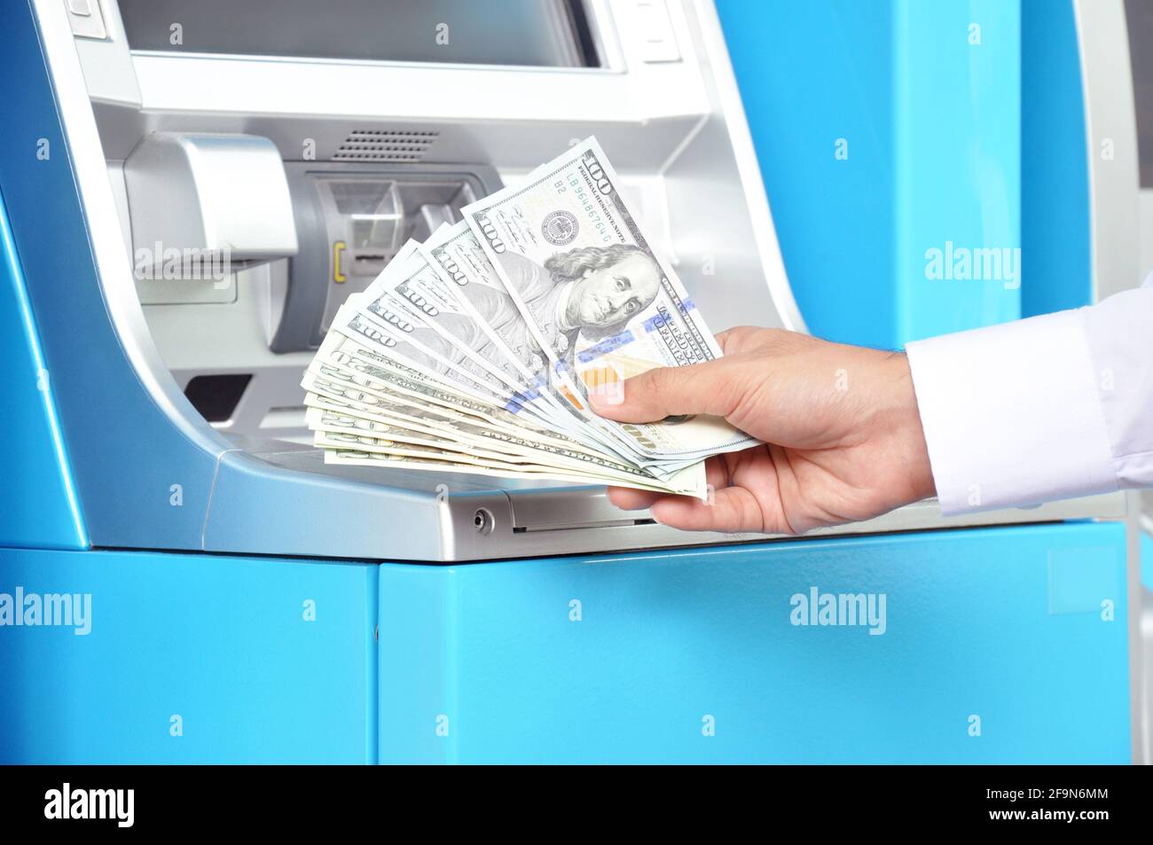 Money - hand holding US dollar banknotes in front of ATM Stock Photo