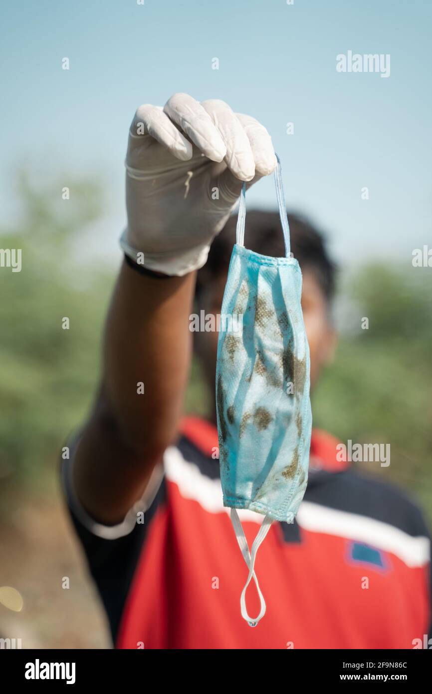 Focus on Hands, Frontline worker or volunteer showing disposable singe use medical face mask to camera after collecting - Concept of discarded medical Stock Photo