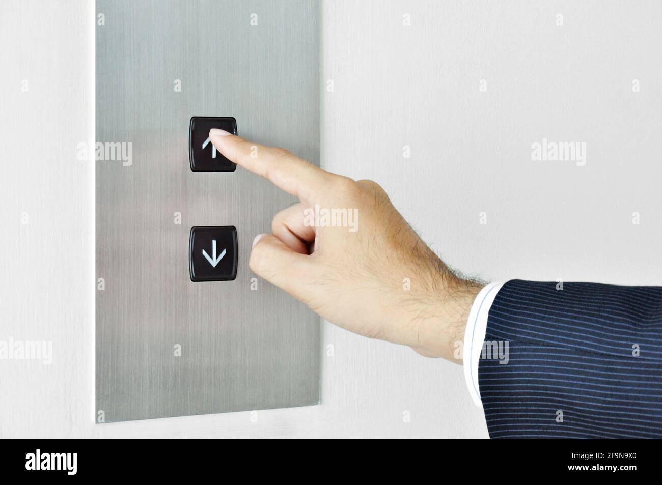 Businessman hand touching going up sign on lift control panel Stock Photo
