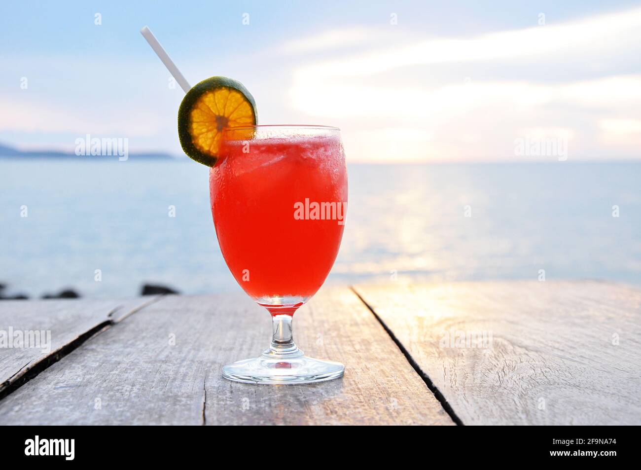 Cocktail drink with orange slice as a garnish on old wooden table & sea water background Stock Photo