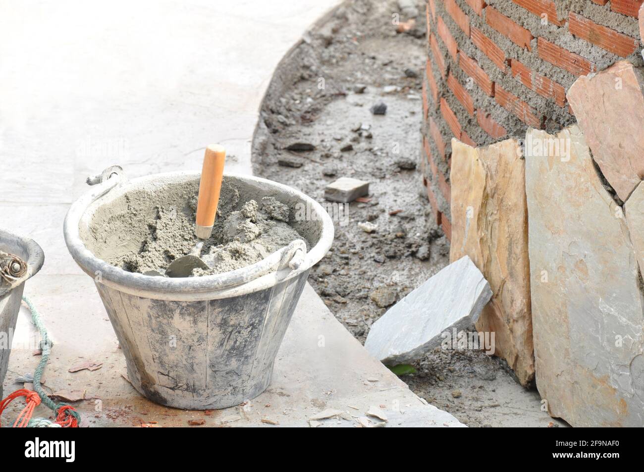 Bucket of mortar with trowel beside constructing brick wall Stock Photo