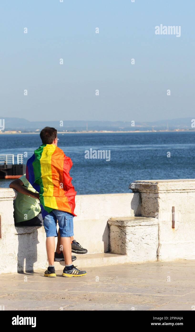 A Gay man covered with the rainbow flag by the Tagus river in Lisbon, Portugal. Stock Photo
