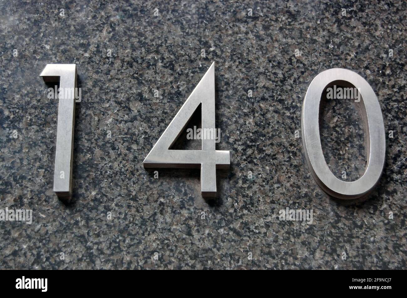 Metal sign showing the number 140 on a marble wall outside an office in