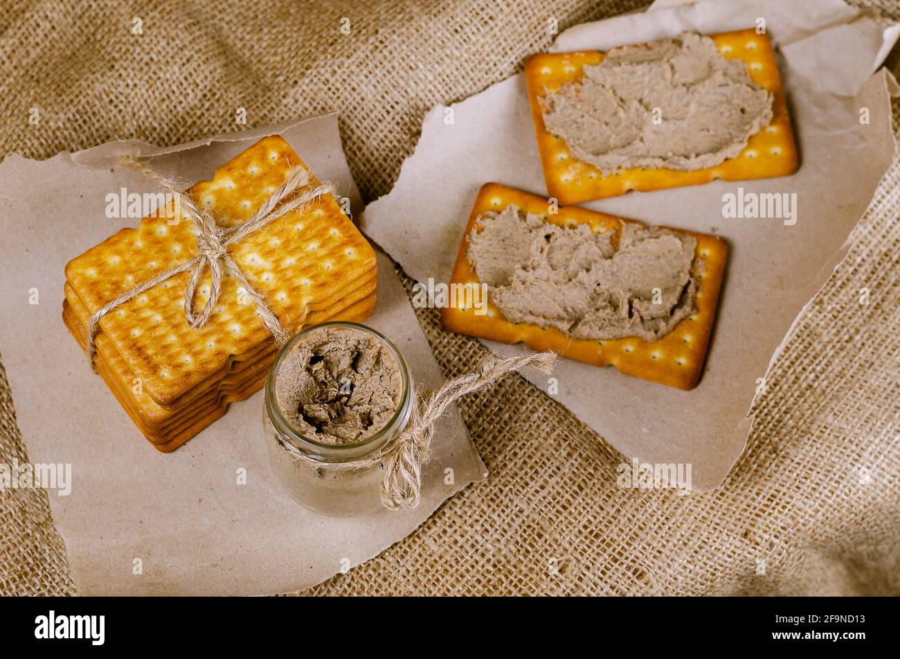 Rectangular crackers and a glass jar of liver pate on sackcloth. Close
