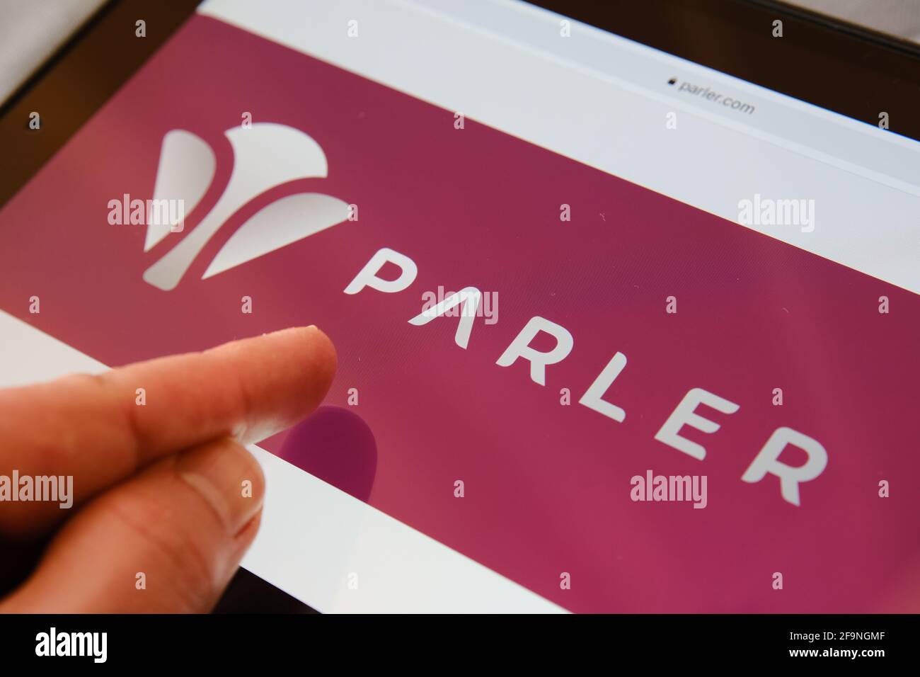 New Parler logo seen on website seen on the screen of Apple ipad and blurred finger pointing at it. Concept. Parler app is conservative social media p Stock Photo