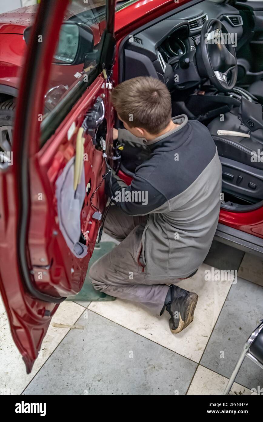 Mechanic guy in automobile service stay on a knees near car door Stock