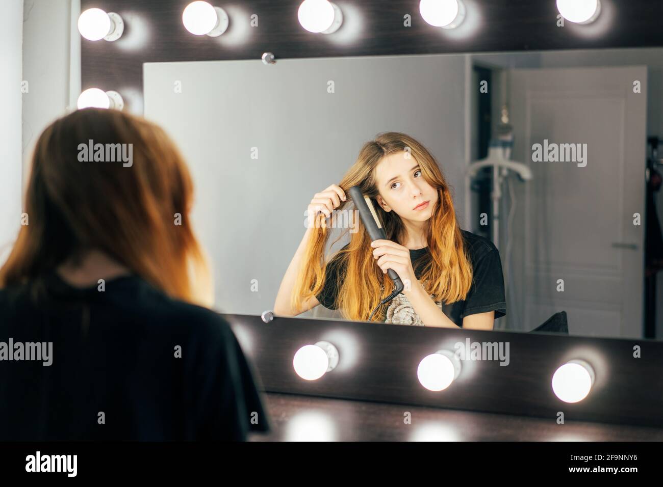Young cute girl teen using a hair straightener on her wavy red hair Stock Photo
