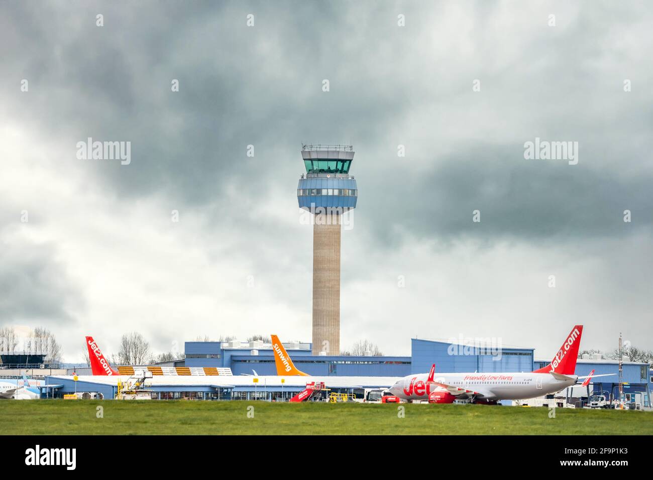 East Midlands Airport radio air traffic Control tower and aircraft planes waiting to depart modern terminal runway with stormy cloud sky behind. Stock Photo