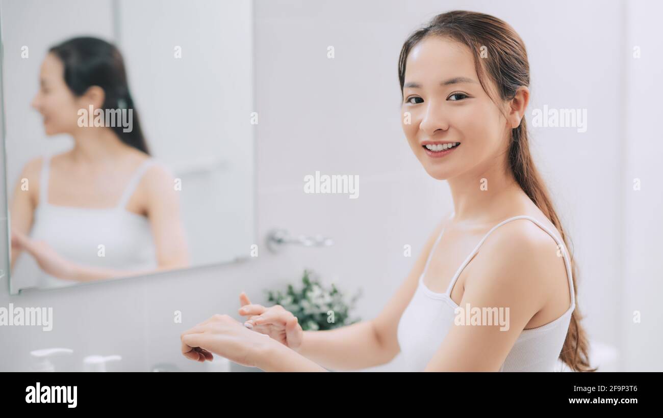 Young woman in towel after shower using body cream. Skin care. Stock Photo