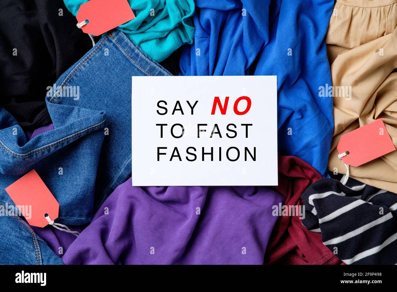 Say No To Fast Fashion sign on paper card over heap of clothes. Fast
