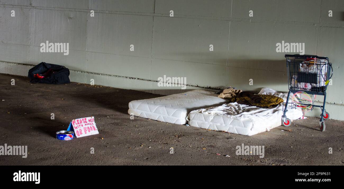 homeless person in berlin built his modest household under the bridge. matress, shopping cart and sign for food donation is the only equipment. Stock Photo