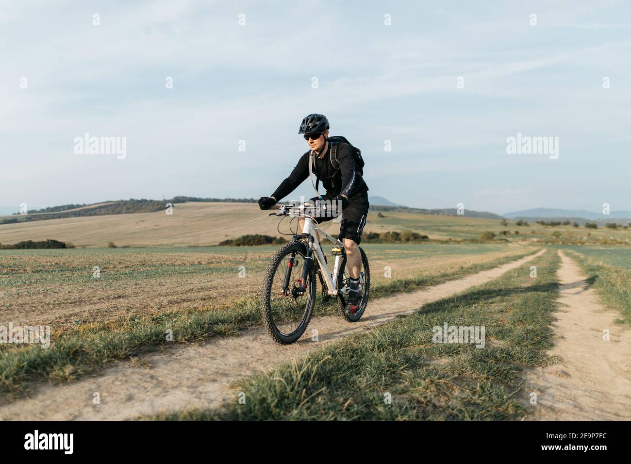 Male cyclist riding bike along country road on clear sunny day. Man mountain biking on dirt track. Stock Photo