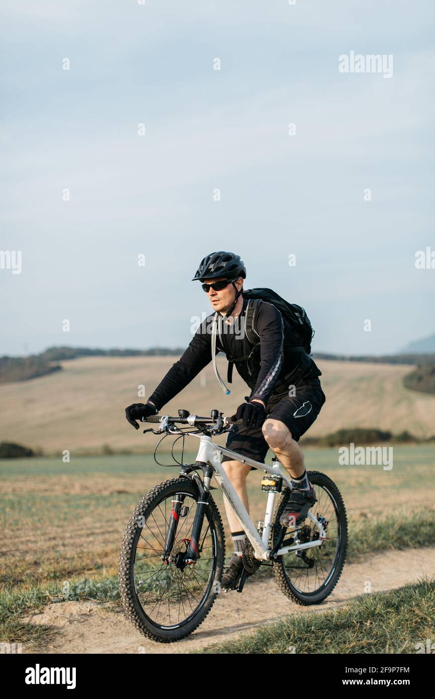 Cyclist cross-country cycling along gravel road on clear sunny day. Man mountain biking on dirt track. Stock Photo
