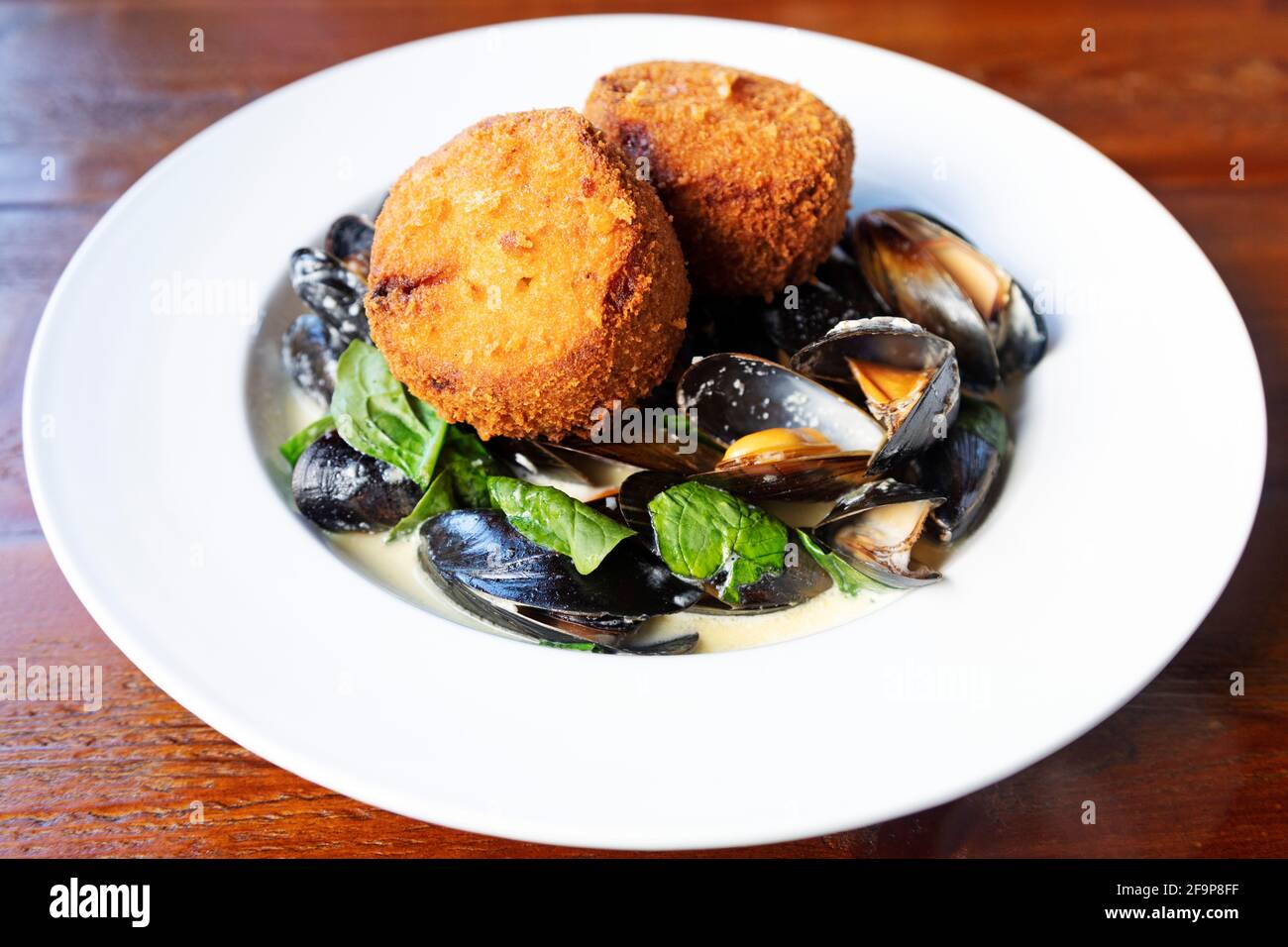 A plate of steamed mussels topped with handmade fishcakes.. The breadcrumbs on the fishcakes are golden in colour. Stock Photo