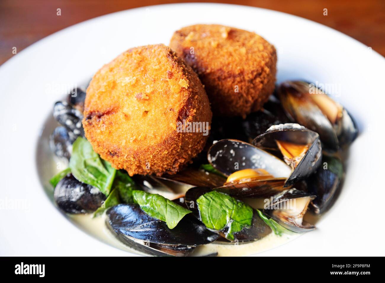 A plate of steamed mussels topped with handmade fishcakes.. The