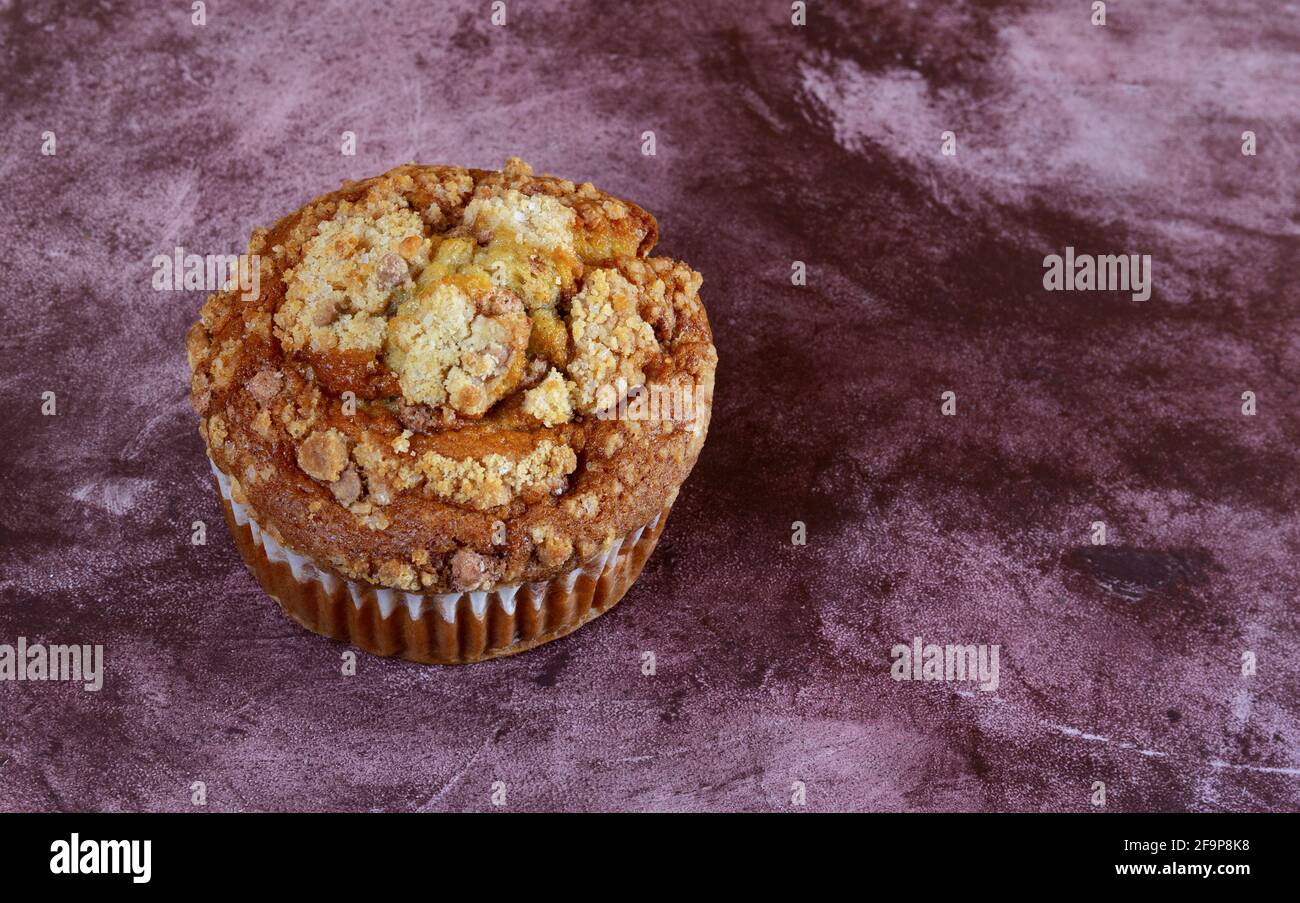 A single cinnamon crumb muffin on a bright maroon tabletop. Stock Photo