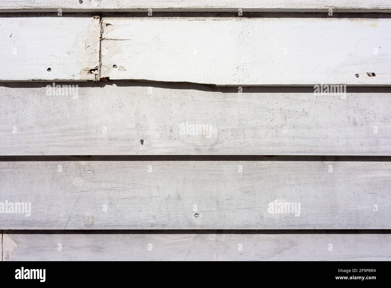 Old clapboard siding painted white with cracks and a broken board in the morning light. Stock Photo