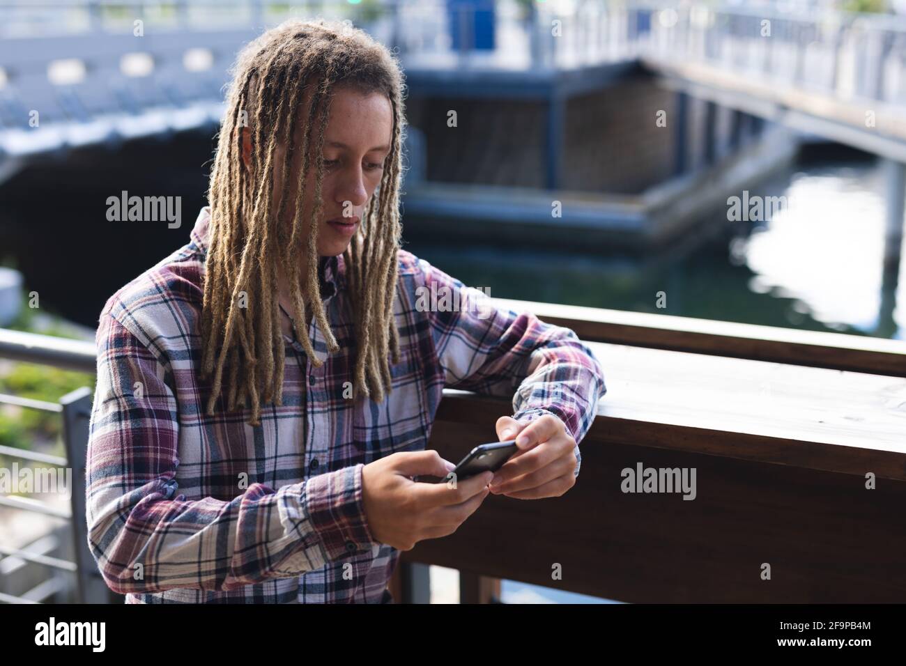 Mixed race man with dreadlocks standing outside cafe using smartphone. digital nomad, out and about in the city. Stock Photo